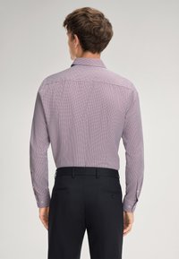 Camicia a maniche lunghe in tessuto bordeaux a fantasia con una piccola stampa geometrica. Polsini con bottoni e colletto. Indossata con pantaloni scuri.
