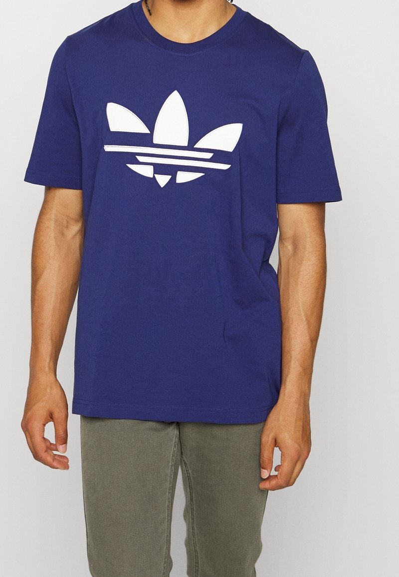 Námořnická modrá bavlněná tričko s velkým bílým logem Adidas se třemi pruhy a listovými akcenty. Krátké rukávy, design s kulatým výstřihem.