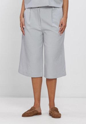 Vidbenede, lysegrå culotte-short med brune slip-on loafers, vist fra midt på taljen til fødderne mod en hvid baggrund.