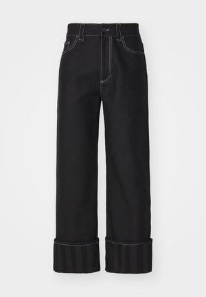 Mustad mustad jalad, kontrastsete valgete õmblustega, viie taskuga disain ja triibulised varrukad. Materjal näib olevat tugev ja siledat tekstuuri.