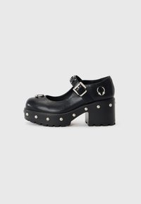 Black leather platform shoes with a round toe, buckle strap, metal accents, and circular stud details along the sole. Chunky block heel.