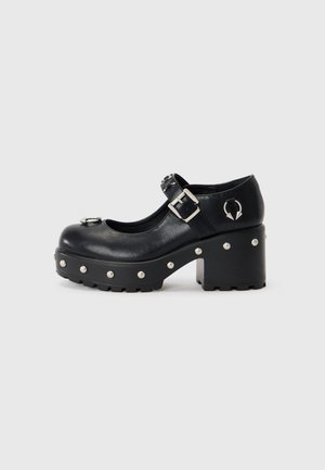 Black leather platform shoes with a round toe, buckle strap, metal accents, and circular stud details along the sole. Chunky block heel.