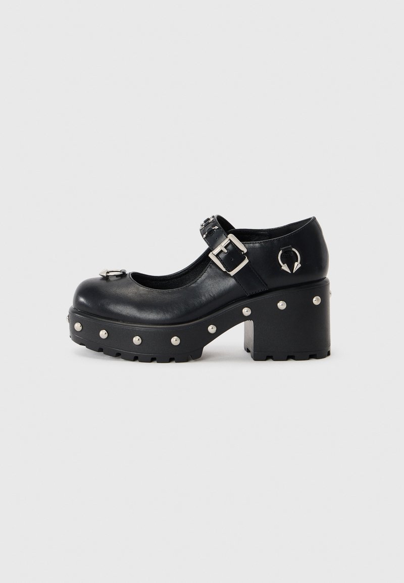 Black leather platform shoes with a round toe, buckle strap, metal accents, and circular stud details along the sole. Chunky block heel.
