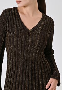 Abito in maglia marrone scuro con texture a coste verticali, arricchito da fili metallici dorati e scollatura a V. Maniche lunghe e silhouette svasata.