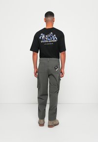 Zwarte T-shirt met kleurrafgrafiek en tekst op de achterkant, gecombineerd met khaki cargo broek met zijzakken en een achterlabel. Bruine laarzen.