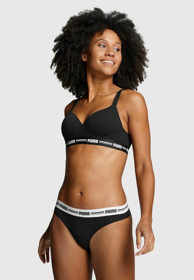 Schwarzer BH mit verstellbaren Trägern und einem weichen, strukturierten Stoff; verfügt über ein weißes, mit Logo bedrucktes Band. Schwarze Unterhosen mit passendem Branding im Bund.