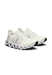 Baskets de sport blanches avec un dessus texturé, un design à lacets et une semelle rembourrée présentant une silhouette ondulée distinctive et des accents noirs.