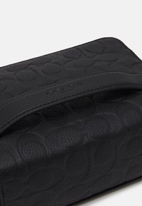Borsa nera in pelle con superficie texturizzata caratterizzata da motivi circolari embossati. Include una tracolla nella parte superiore, semplice e di forma rettangolare.