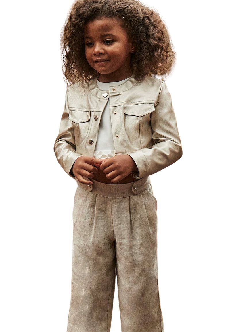 Giacca cropped in pelle beige chiaro con due tasche frontali, abbinata a pantaloni larghi in lino marrone chiaro con una vita alta e pieghe.