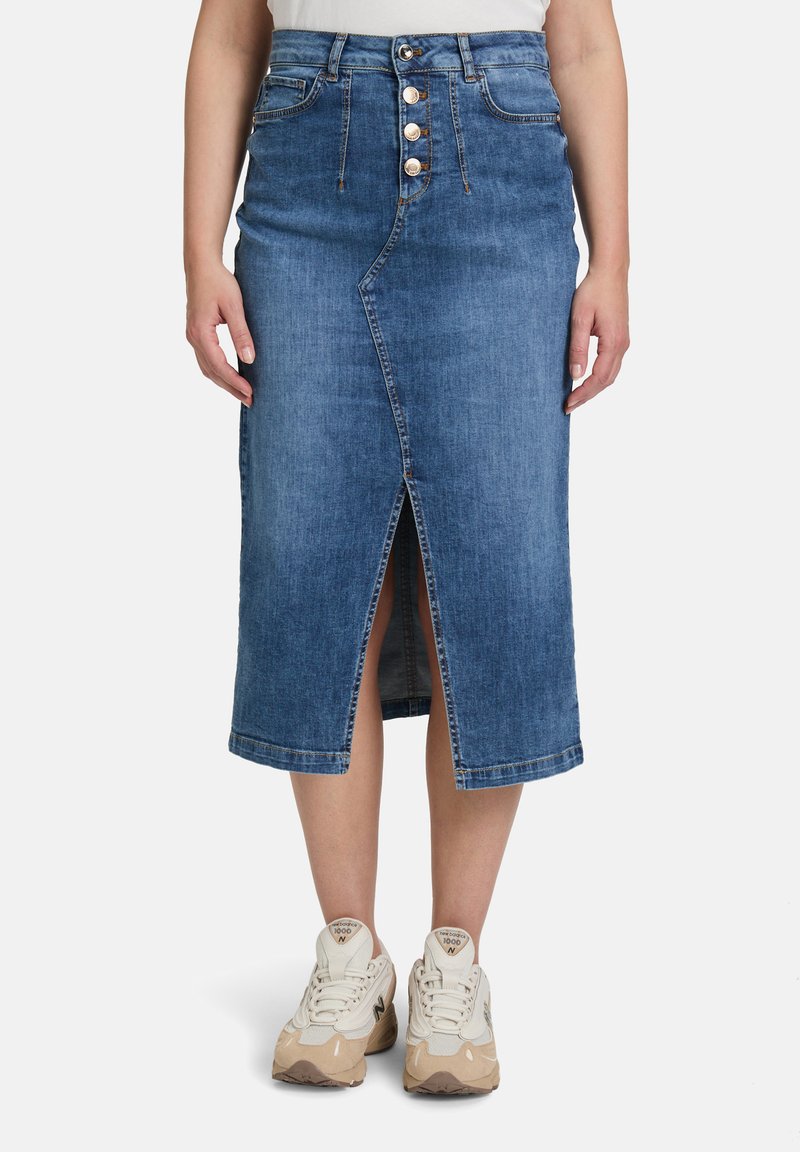 Jupe midi en jean de couleur bleu clair avec une fente à l'avant et une fermeture à cinq boutons. Dotée de passants de ceinture et d'un design légèrement décoloré. Portée avec des baskets beiges.