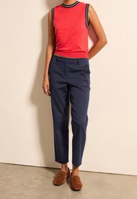 Czerwony top bez rękawów z granatowym wykończeniem, paired z granatowymi spodniami o dopasowanym kroju i brązowymi zamszowymi butami wsuwanymi. Ubranie posiada dopasowaną sylwetkę.