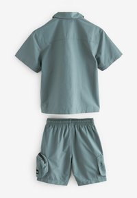 Ensemble comprenant une chemise à manches courtes et un short en tissu bleu-vert doux. La chemise est dotée d'un col; le short a une taille élastique et des poches cargo.