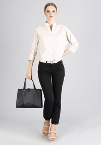 Camisa de botón color beige claro, jeans skinny negros, bolso estructurado negro con herrajes dorados, y sandalias beige con tiras.