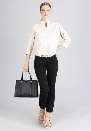 Camisa de botón color beige claro, jeans skinny negros, bolso estructurado negro con herrajes dorados, y sandalias beige con tiras.