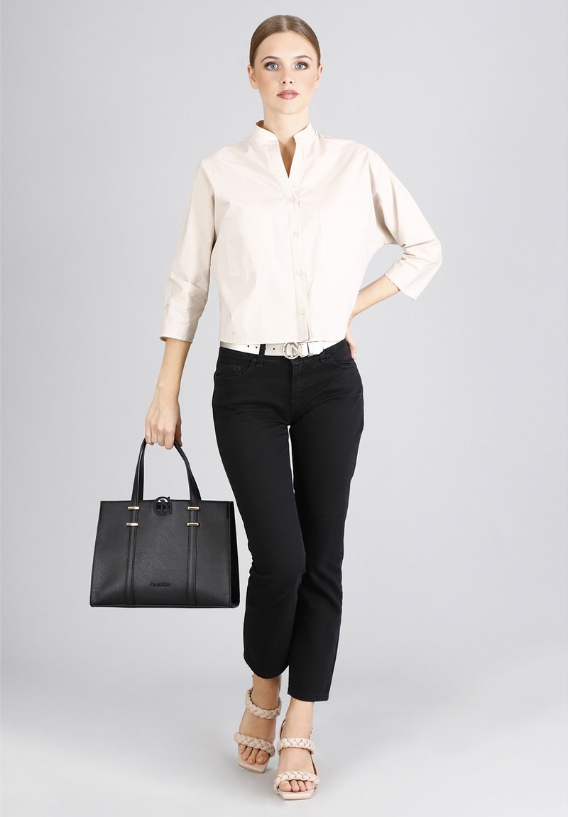 Camisa de botón color beige claro, jeans skinny negros, bolso estructurado negro con herrajes dorados, y sandalias beige con tiras.