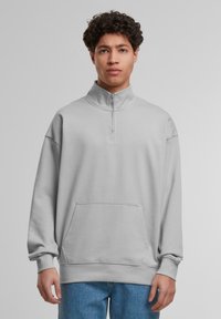 Light gray quarter-zip sweatshirt with long sleeves, kangaroo pocket, and ribbed cuffs. Made of soft fabric with a relaxed fit.