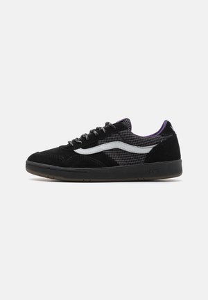 Sneaker nere in suede con un pannello in tessuto testurizzato, caratterizzate da una striscia iconica bianca, suola in gomma nera e dettagli viola sul colletto.