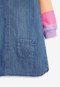 Vestido de mezclilla con un bolsillo frontal, combinado con un sudadera de manga larga que presenta bloques de color naranja, rosa y púrpura.