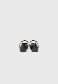 Ballerines en cuir noir avec une sangle réglable et des détails en métal doré. Bout arrondi et texture lisse. Design minimaliste. Vue de dos.