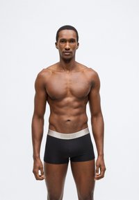 Fekete, rugalmas anyagból készült boxeralsó, bézs elasztikus derékrésszel, márkalogóval. Simogató tapintású, testhez simuló szabás.