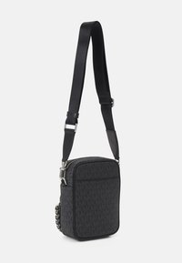 Borsa a tracolla nera realizzata in materiale testurizzato, con chiusura con zip, tracolla regolabile e motivo logo prominente. Forma rettangolare compatta.
