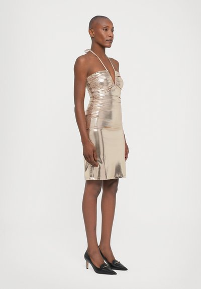 Rochie metalică aurie, cu gât halter și design strâns; până la genunchi. Purtați-o cu pantofi cu vârf ascuțit negri, cu accente aurii. Textură netedă.
