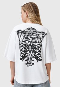 T-shirt bianco oversize con stampa grafica di una gabbia toracica nera sul retro, maniche corte e vestibilità rilassata.