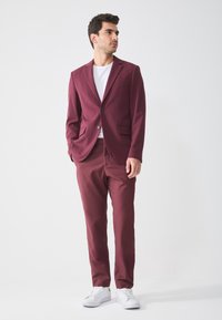 Traje burdeos con blazer ajustado y pantalones a juego, de corte slim, tejido ligero, combinado con una camiseta blanca y zapatillas blancas.