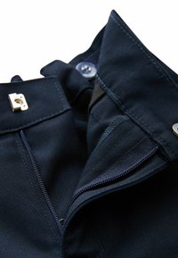 Tume-sinine kangas siledal tekstuuril, millel on krae, nööpidega kinnis ja küljes tõmblukk, mille ava juures on nähtavad hõbedased detailid.