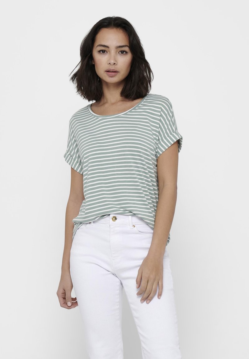 T-shirt à manches courtes rayé en vert clair et blanc, fabriqué en tissu doux, avec un col large et une coupe décontractée, associé à un jean blanc.