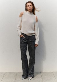 Licht beige, cold-shoulder trui met een relaxte pasvorm; gecombineerd met donkere, met pailletten bezette flared broeken. Puntige witte hakken met metallic accenten.