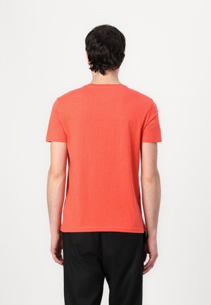 Koszulka z krótkim rękawem w jasnym kolorze koralowym, wykonana z miękkiej bawełny, z luźnym krojem i klasycznym okrągłym dekoltem. Brak wyraźnych wzorów lub akcentów.