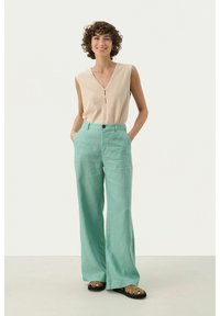 Un haut sans manches beige clair avec un décolleté en V et des boutons, associé à un pantalon large vert menthe et des sandales noires.