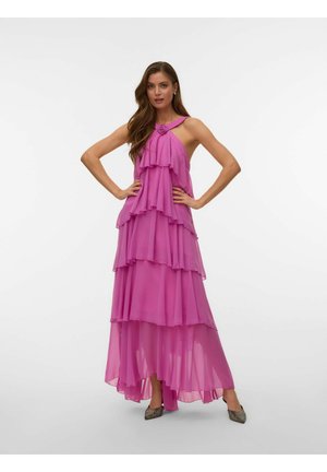 Kvinne i en flowing lagdelt fiolett halterneck-kjole med blomsterdetaljer, hendene på hoftene, iført skinnende spisse hæler.