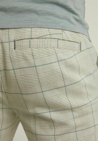 Beiga plädbyxor med ett strukturerat tyg med rutmönster i ljusblått och mörkgröna accenter, samt en detalj med bakficka.