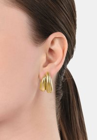 Guldiga dropformade örhängen som visas på örsnibben; slät, glänsande yta med två överlappande droppar som taperar i formen.