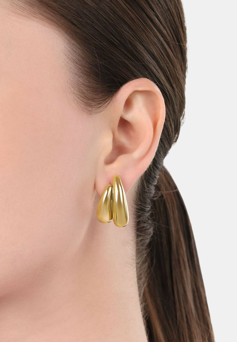 Guldiga dropformade örhängen som visas på örsnibben; slät, glänsande yta med två överlappande droppar som taperar i formen.