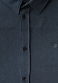 Marinblå pikétröja i bomull, med klassisk krage, fem svarta knappar och en liten logotag på vänster sida.