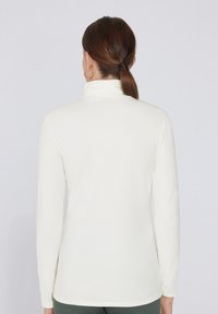 Top blanco de manga larga con cuello simulado y textura suave. Ajuste slim con aberturas laterales en el dobladillo, confeccionado en una tela elástica y suave.