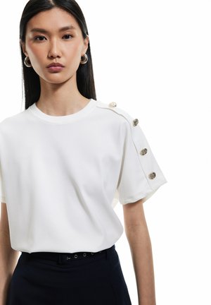 Witte korte mouwen shirt met een ronde halslijn en zilveren knoopaccenten op de schouders. Glad materiaal, casual pasvorm, gecombineerd met donkere broek.