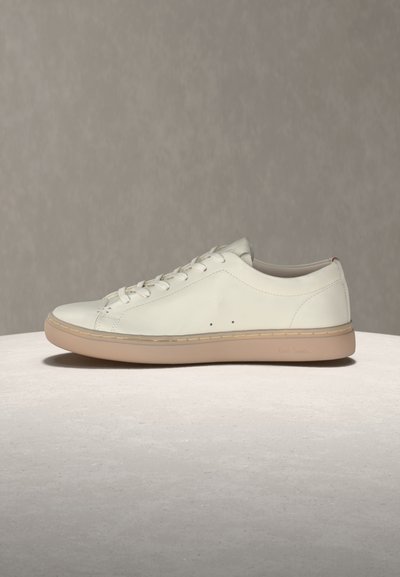 Low-top white leather sneaker with beige rubber sole, lace-up front, minimal stitching, and two small side ventilation holes on neutral background.