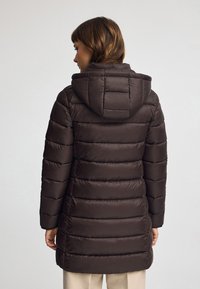 Brun vadderad jacka med huva, med horisontella quiltade sektioner. Slät textur och enhetlig färg ökar värmen och skyddet.