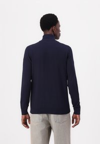 Navy sweater with a mock neck, long sleeves, and ribbed cuffs, paired with light-colored jeans; smooth texture, fitted design.