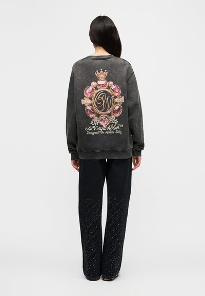 Σκούφο, υπερμεγέθη φούτερ με μοτίβο από πολύτιμους λίθους στην πλάτη. Συνδυάζεται με μαύρο παντελόνι με διαγώνιο διακοσμητικό μοτίβο με τρουκς.