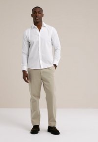 Biała koszula na guziki, beżowe spodnie i ciemne buty. Koszula ma długie rękawy i standardowy kołnierzyk, a spodnie mają prosty krój.