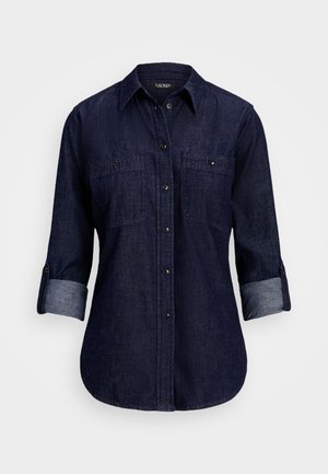 Chemise en jean bleu foncé à boutons, manches longues retroussées aux trois quarts et deux poches poitrine à boutons.