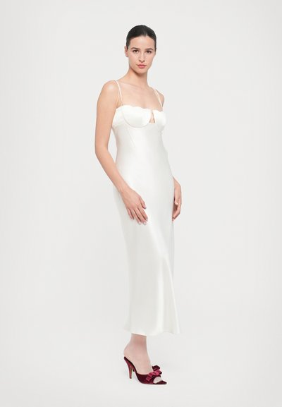 Vestido de satén blanco con un corsé ajustado que presenta un escote festoneado y tirantes delgados. Combinado con tacones abiertos burdeos con lazos.