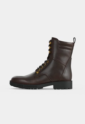 Dark brown leather lace-up combat boot with black rubber sole and gold eyelets, mid-calf height and branded sole edge.