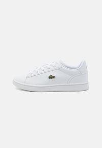 Hvite sneakers med en glatt syntetisk overdel, rund tå, snøring foran og grønt krokodille-logo på siden. Enkel, klassisk design.
