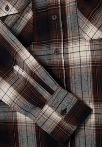 Bruine en crèmekleurige geruite flanellen shirt met knoopsluiting, met contrasterende kleuren, een kraag en een zakdetail op de borst.